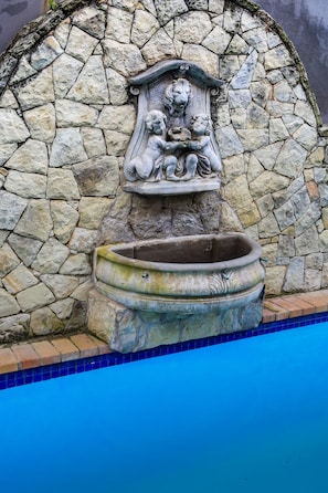 Un muro de piedra con una fuente decorativa y una piscina.