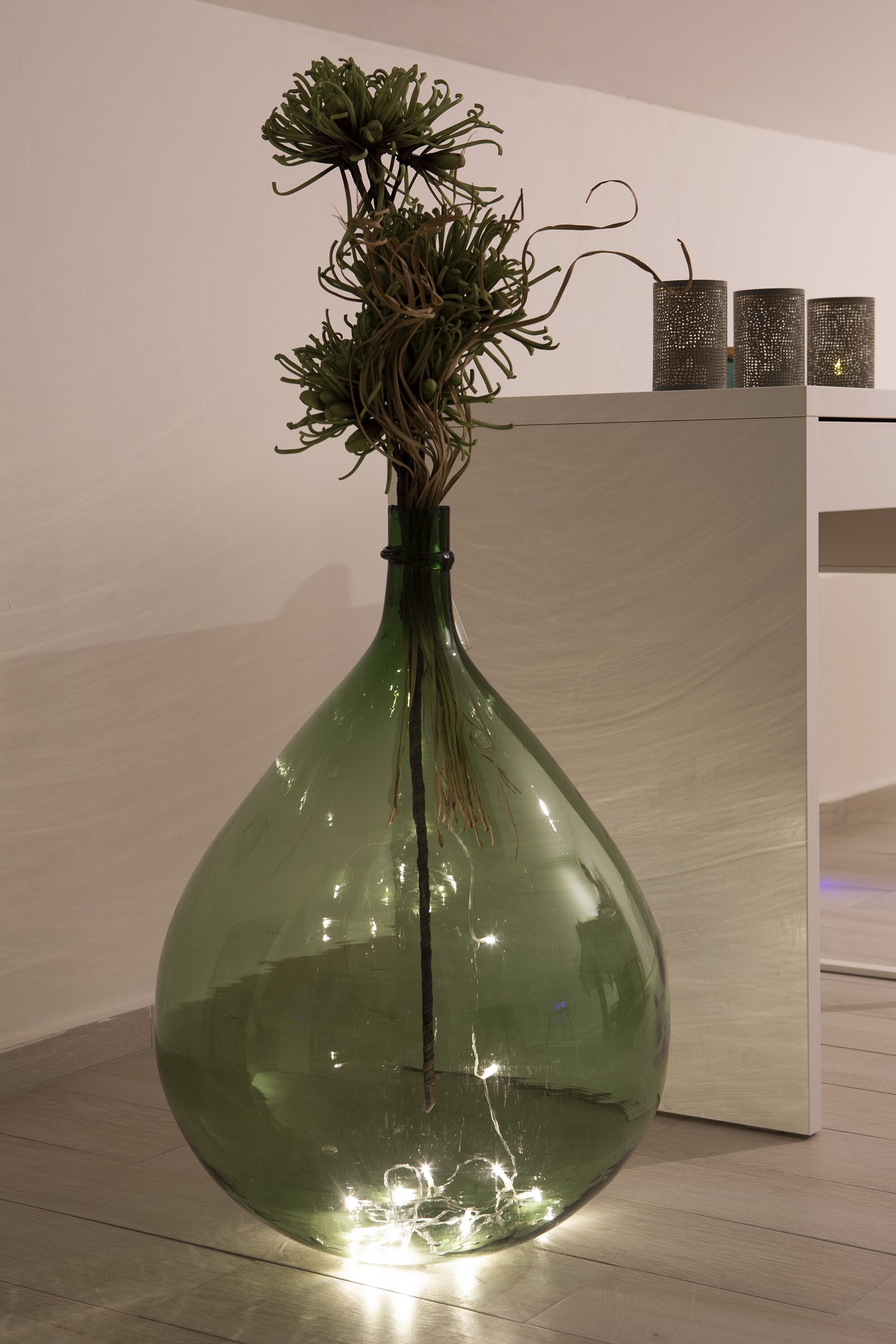 A large green glass vase with a plant on a wooden floor.