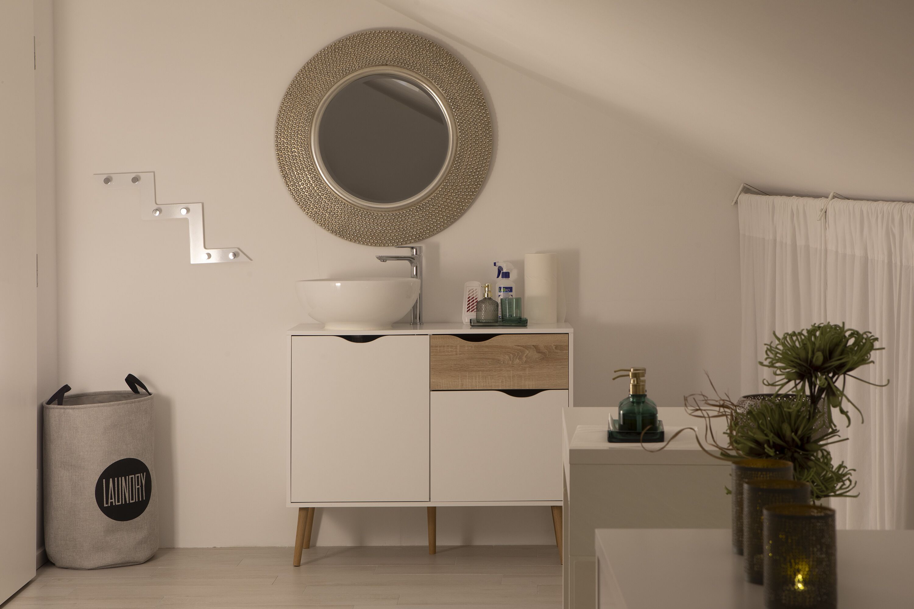 A modern bathroom with a white vanity, a round mirror, a towel rack, and a small plant.