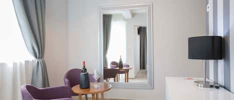 A modern hotel room with a large mirror, a wooden table with a wine bottle and glass, purple chairs, a desk with a lamp, and a telephone.