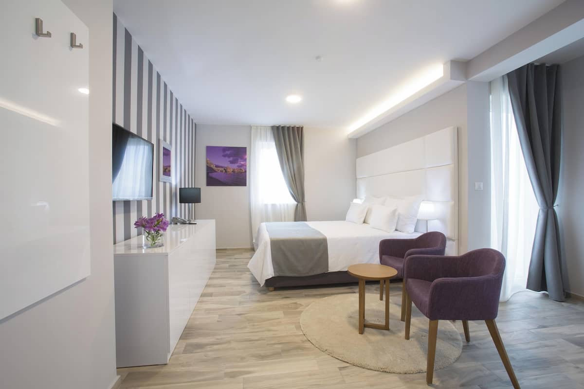 A modern hotel room with a bed, a desk, a chair, and a TV.