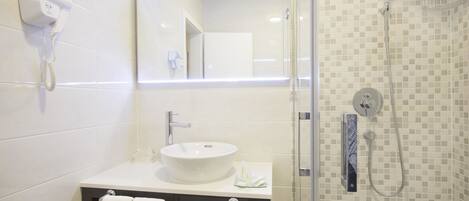 A bathroom with a white sink, a towel rack, a hairdryer, and a shower with a tiled wall.