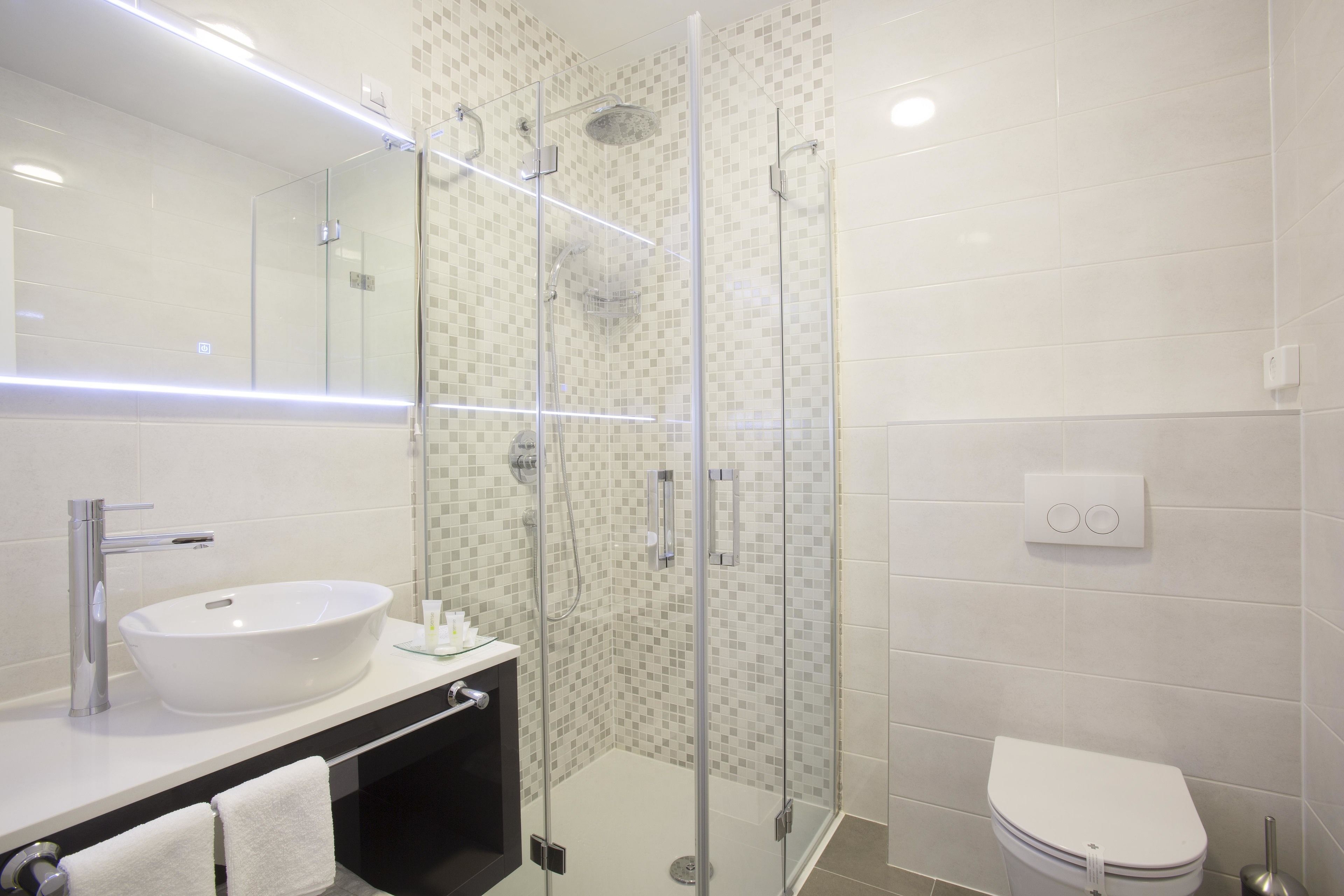 Un baño moderno con ducha de vidrio, lavamanos blanco y un inodoro.