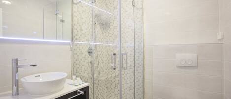 Un baño moderno con ducha de vidrio, lavamanos blanco y un inodoro.