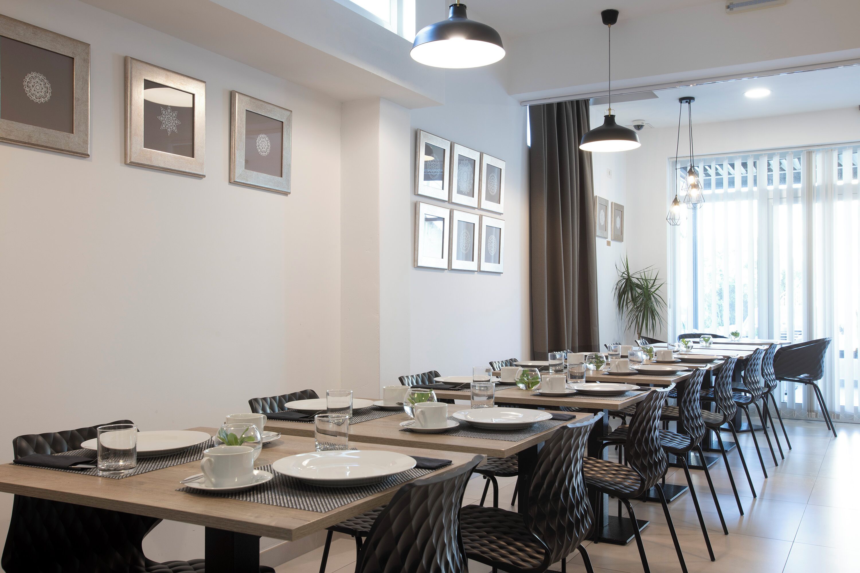 A modern dining area with long tables, black chairs, and framed artwork on the walls.