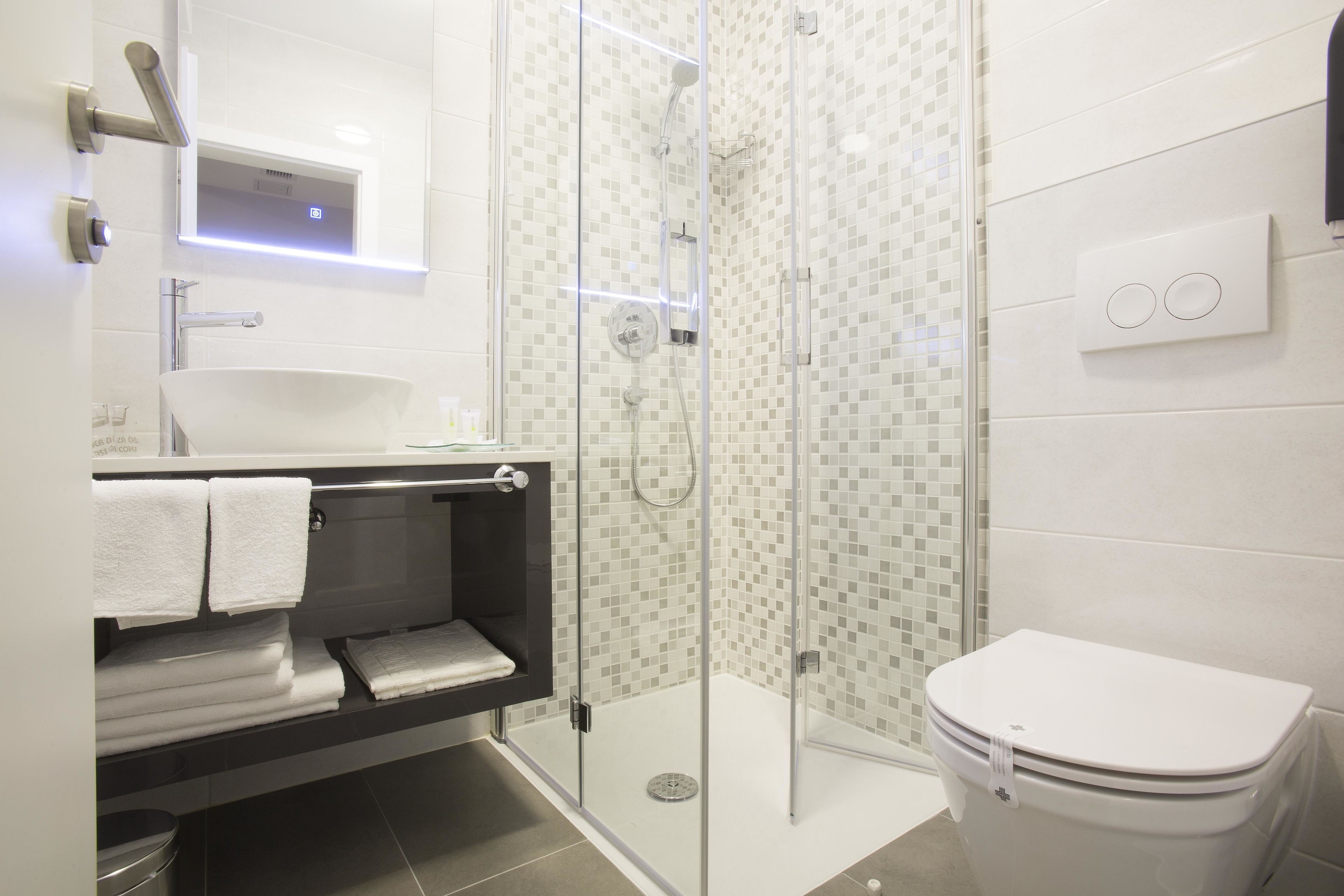 Ein modernes Badezimmer mit einer in Glas abgeschirmten Dusche, einem weißen Waschbecken und einer Toilette.