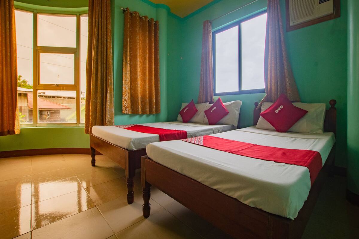 Une chambre d’hôtel avec deux lits, une fenêtre avec des rideaux et un sol carrelé.