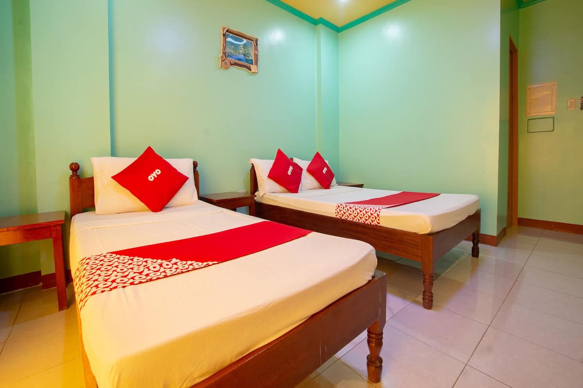 Une chambre d’hôtel avec deux lits, chacun agrémenté d’un oreiller rouge et d’une couverture rouge.