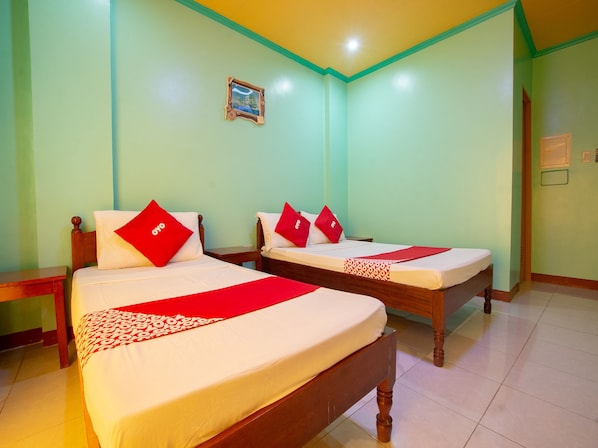 A hotel room with two beds, each with a red 'oyo' pillow, white bedding, and a red and white patterned bed runner.