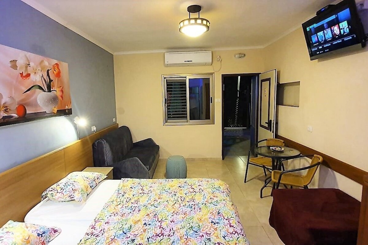 A hotel room with a bed, a desk, a chair, a TV, and a painting on the wall.