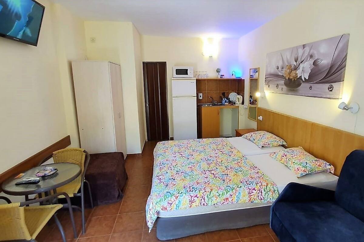 A hotel room with a bed, a sofa, a small table with chairs, a microwave, a refrigerator, and a television on the wall.