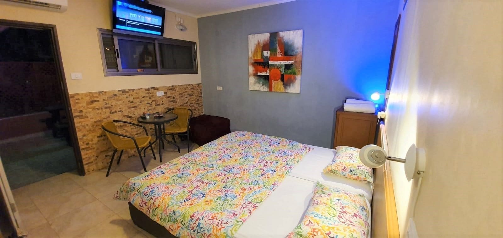 Ein Hotelzimmer mit einem Bett, einem kleinen Tisch, zwei Stühlen, einem Fernseher und einem Bild an der Wand.