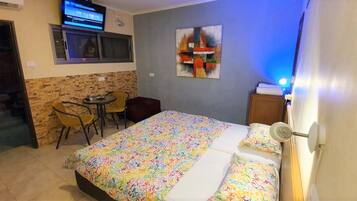Ein Hotelzimmer mit einem Bett, einem kleinen Tisch, zwei Stühlen, einem Fernseher und einem Bild an der Wand.