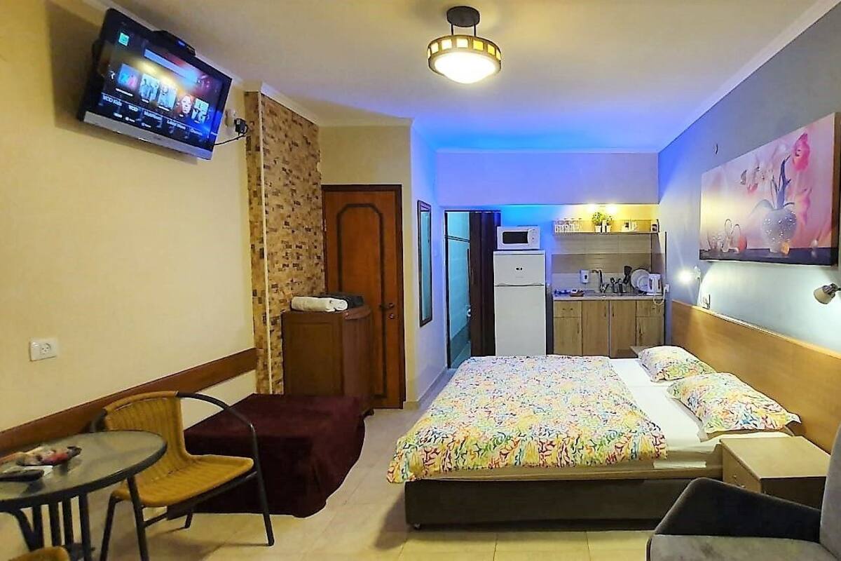 A hotel room with a bed, a TV, a desk, a chair, and a kitchenette.