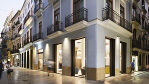 A building with multiple storefronts, large glass windows, and balconies with black railings. - One Shot Mercat (Valencia)