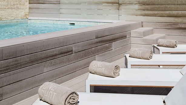 A poolside area with lounge chairs and towels, a wooden wall, and a clear pool. - One Shot Mercat (Valencia)