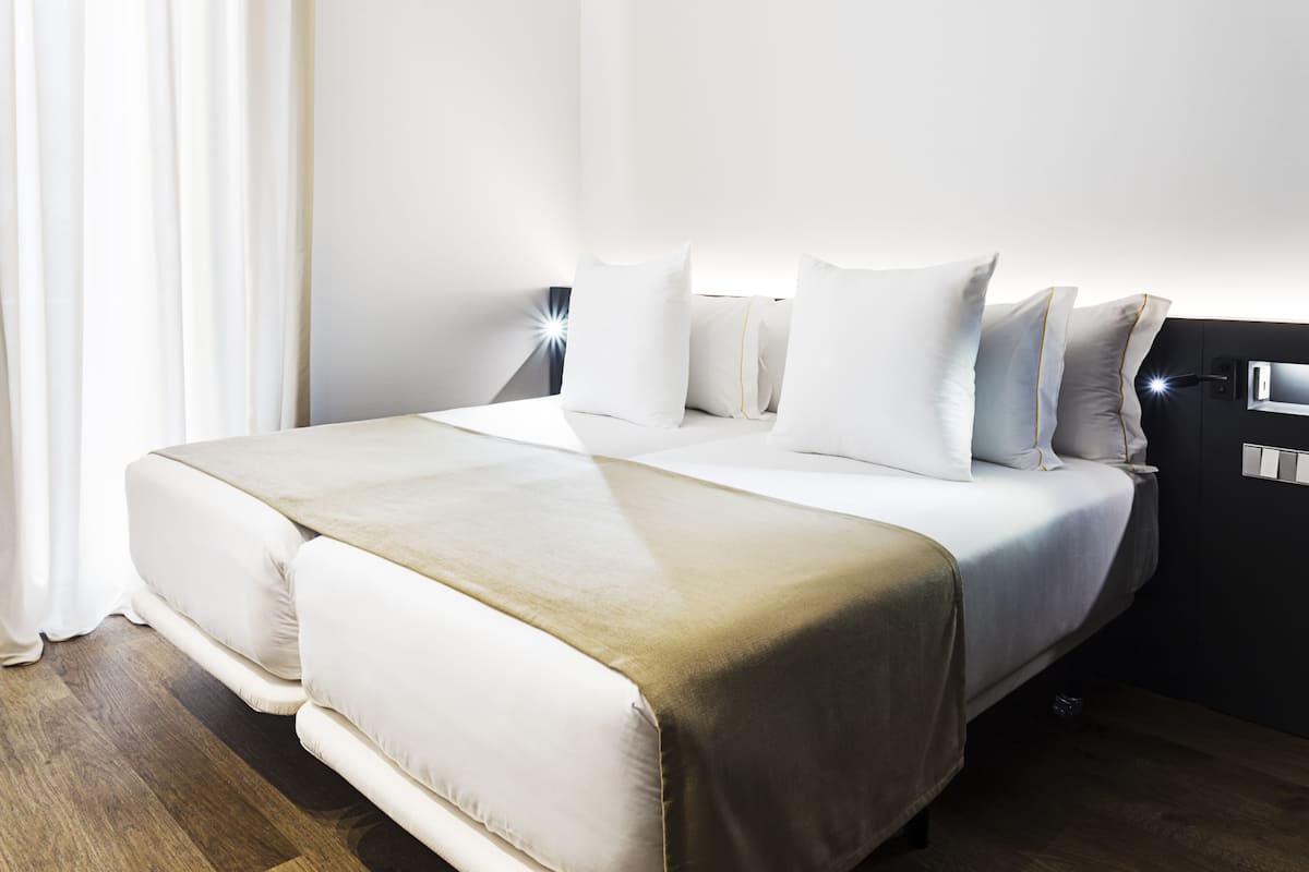 A modern hotel room with a large bed, white bedding, and a bedside table with a lamp.