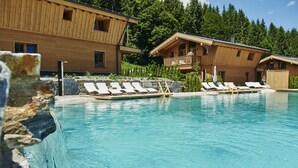A wooden cabin with a pool, lounge chairs, and a stone wall. - LA SOA Chalets & Eventlodge (Schattwald)