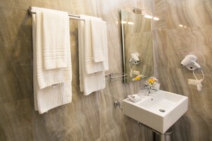 Un bagno con una parete in marmo, un lavandino bianco e due asciugamani appesi a un portaserviti.