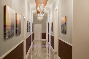 Un corridoio con un lampadario, opere d'arte alle pareti e una porta in fondo.