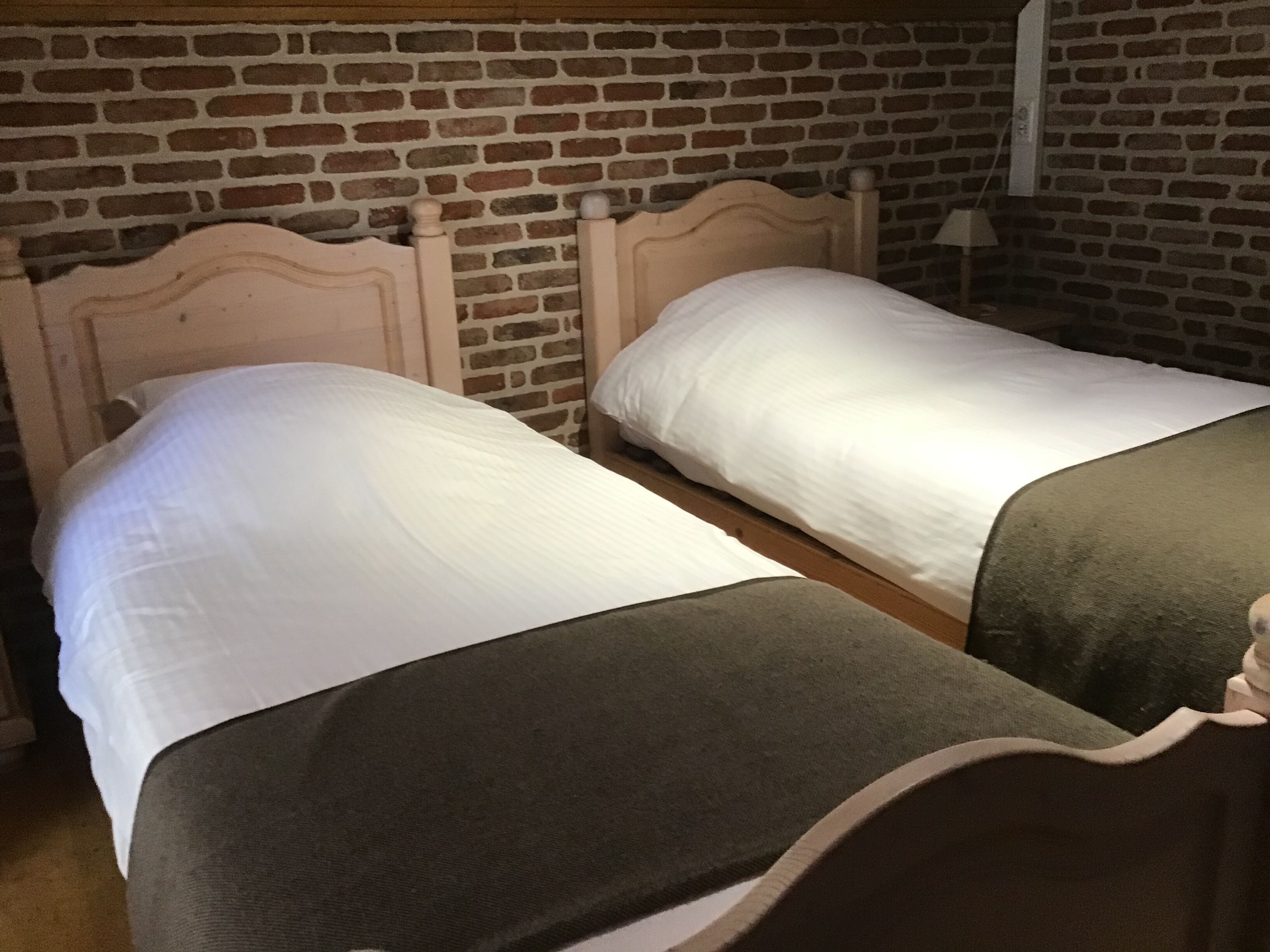 A room with two beds against a brick wall, each with a wooden headboard and white bedding.