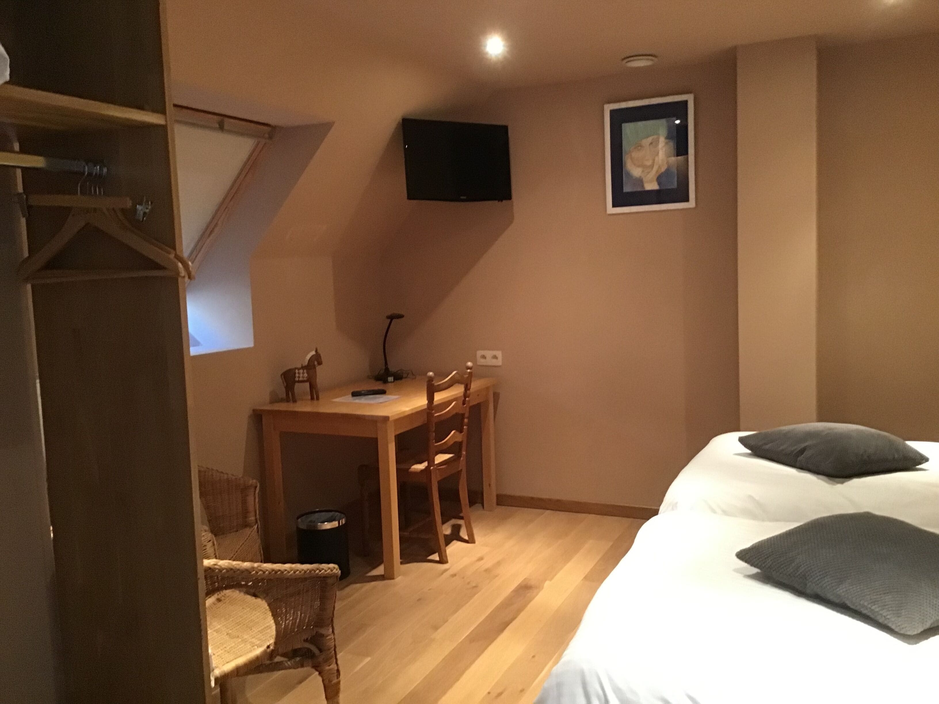 Ein Schlafzimmer mit einem Bett, einem Schreibtisch, zwei Stühlen, einem Fernseher und einem gerahmten Bild an der Wand.