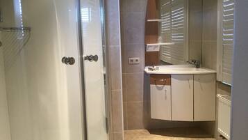 Un baño con cabina de ducha de vidrio, un lavamanos blanco y un espejo sobre él.
