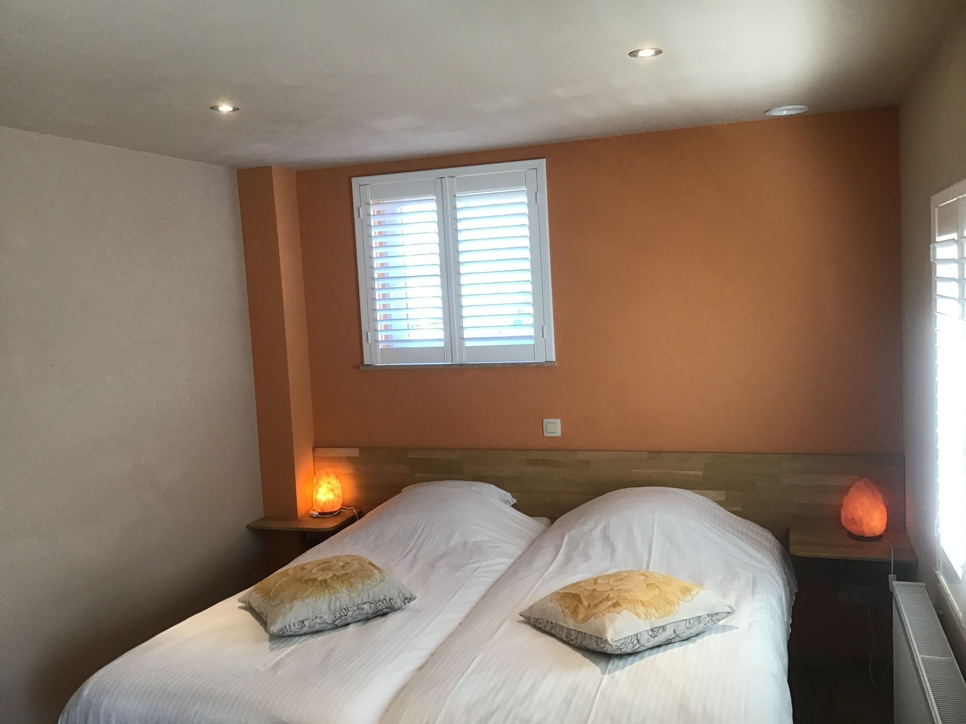 A bedroom with two single beds, a window with blinds, a bedside lamp, and a heater.