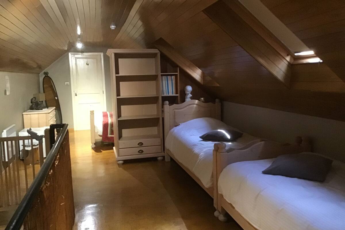 A bedroom with a sloped ceiling, a wooden bed, a bedside table, a wardrobe, and a mirror.