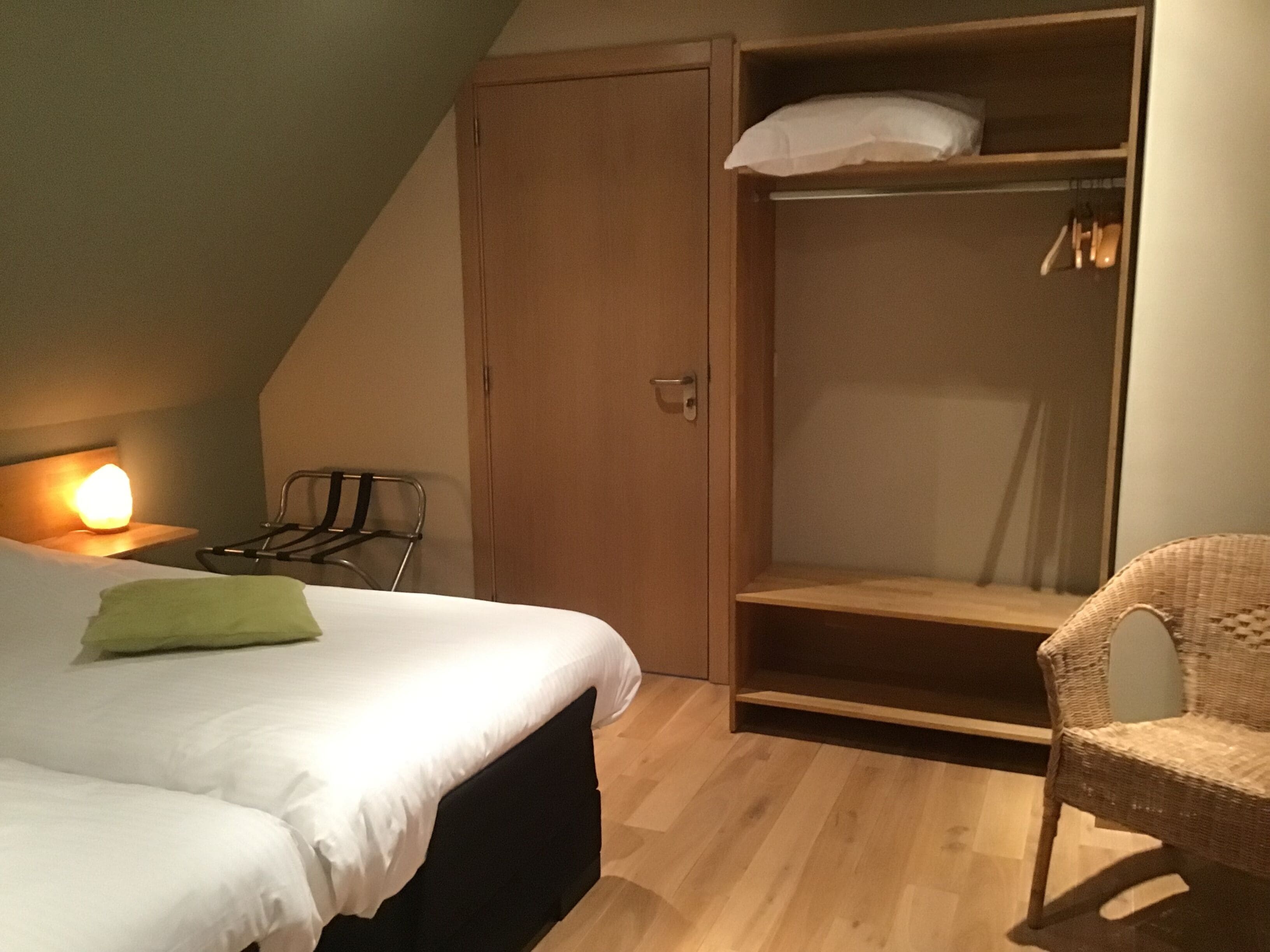 A bedroom with a bed, a wardrobe, a chair, and a bedside table with a lamp.