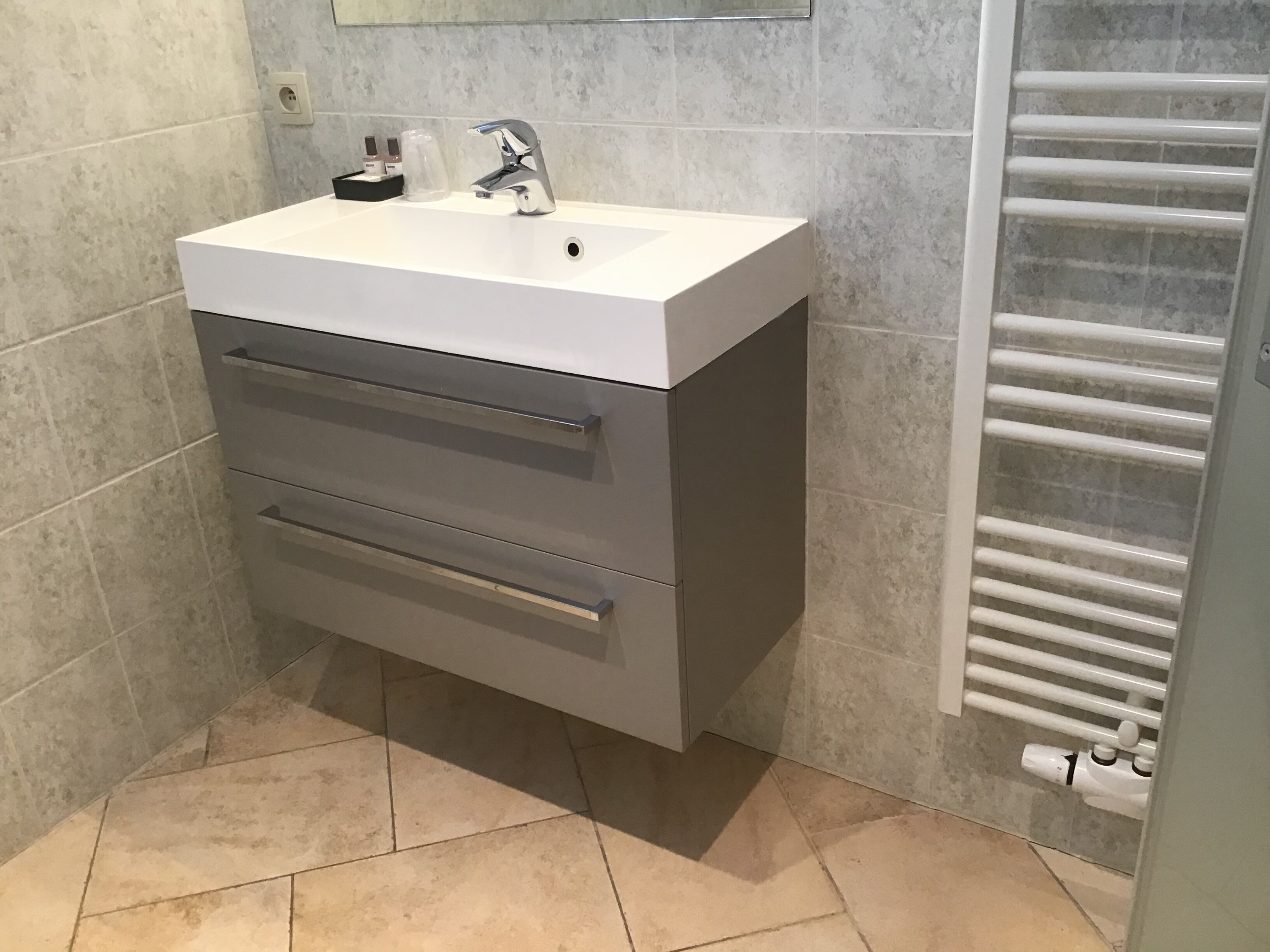 Une salle de bain avec un lavabo blanc, un meuble gris et un porte-serviettes.