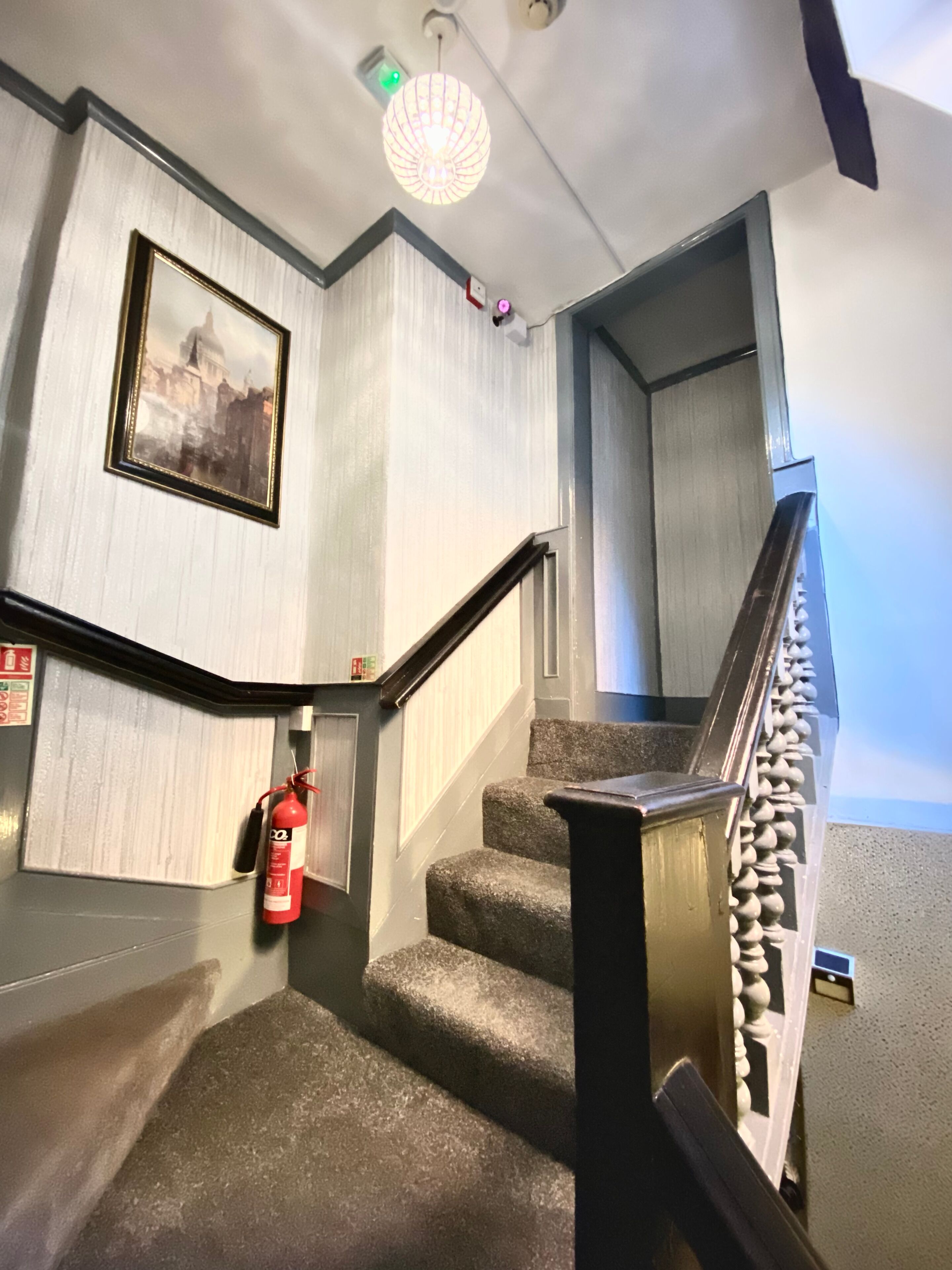 A staircase with a fire extinguisher, a framed picture, and a light fixture.