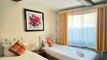 A hotel room with two single beds, a framed picture on the wall, and a window with curtains.