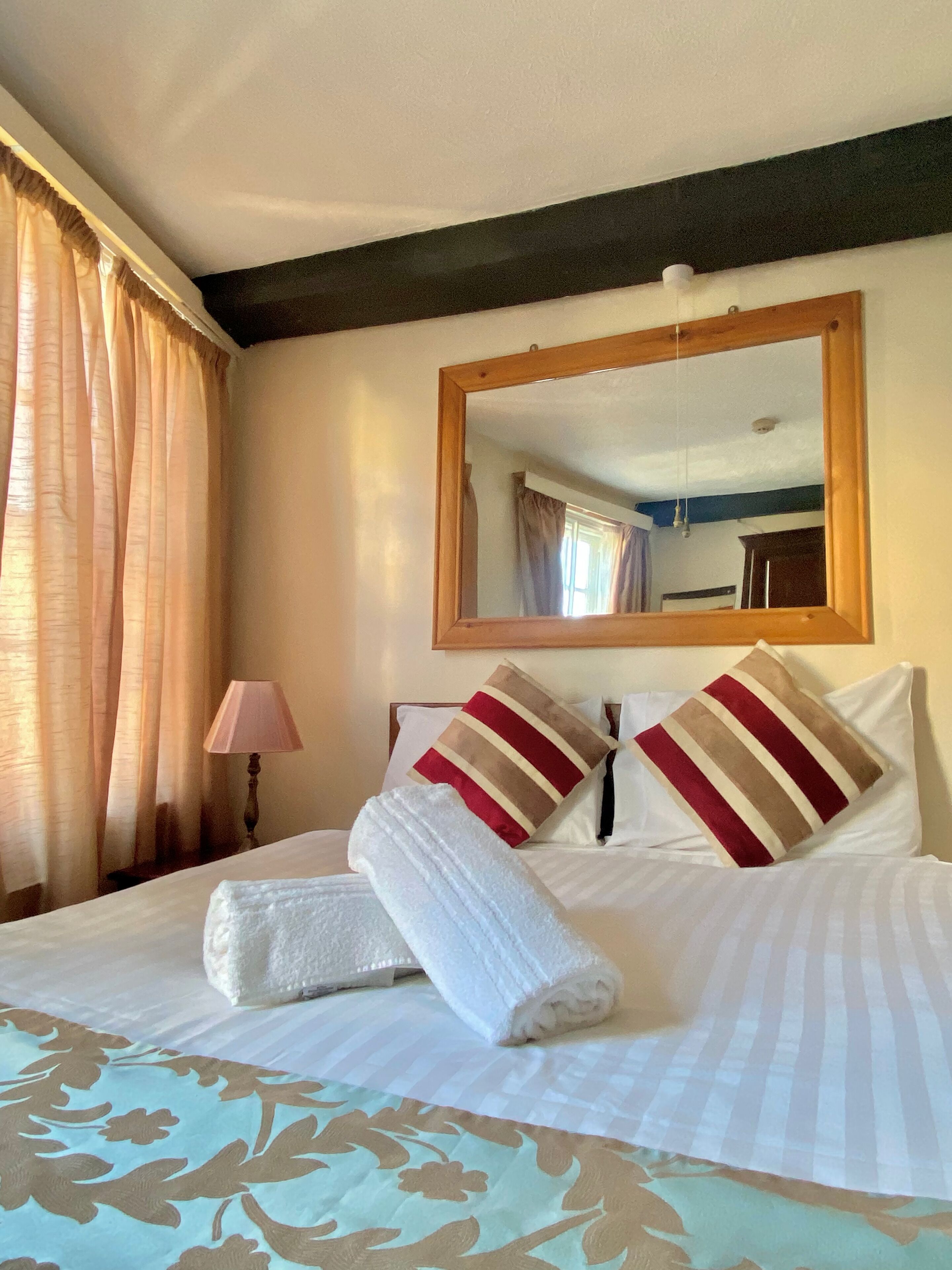 A neatly made bed with striped pillows and a folded towel, a bedside lamp, and a mirror on the wall.