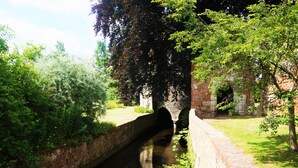 A narrow water channel with a brick bridge, surrounded by lush greenery and a brick building. - Greyfriars Lodge (Canterbury)