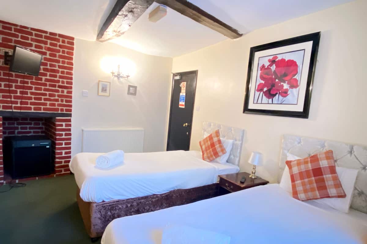 Habitación de hotel con dos camas, una chimenea, un cuadro con flores y una puerta con un cartel.