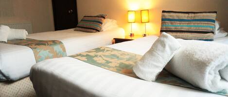 Two single beds with floral-patterned bedspreads, a nightstand with two lamps, and a door with a sign.