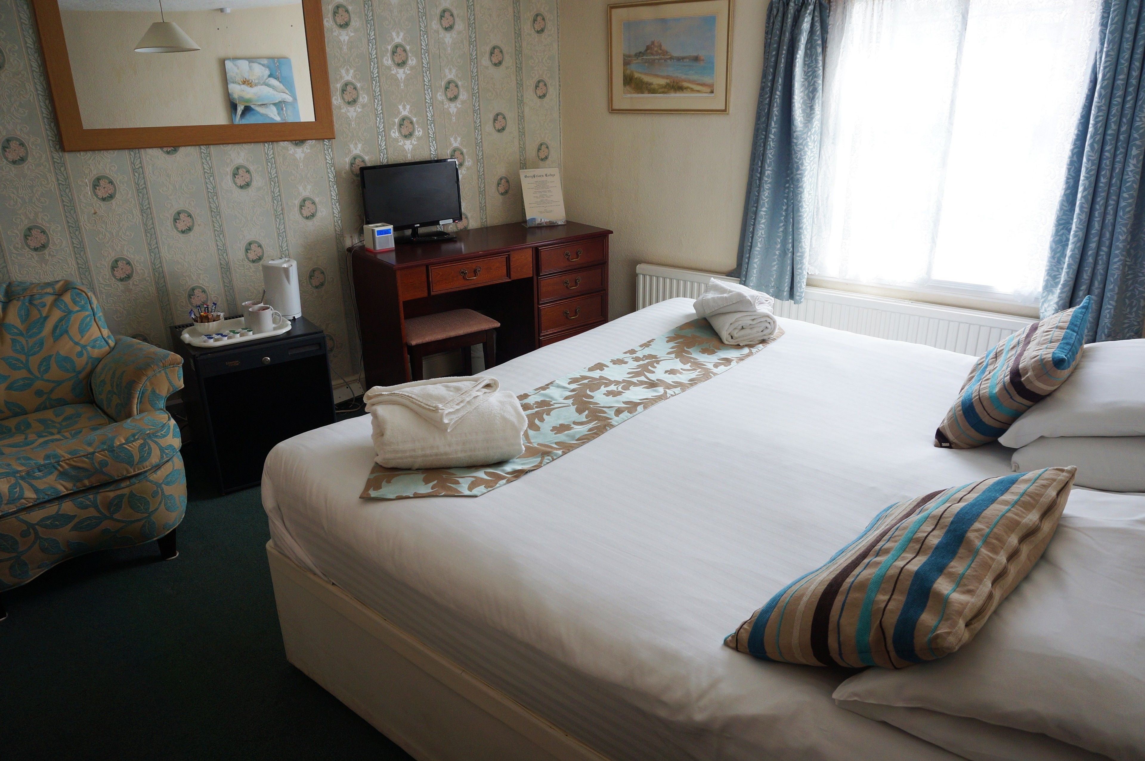A hotel room with a bed, a desk with a computer, a chair, and a window with curtains.