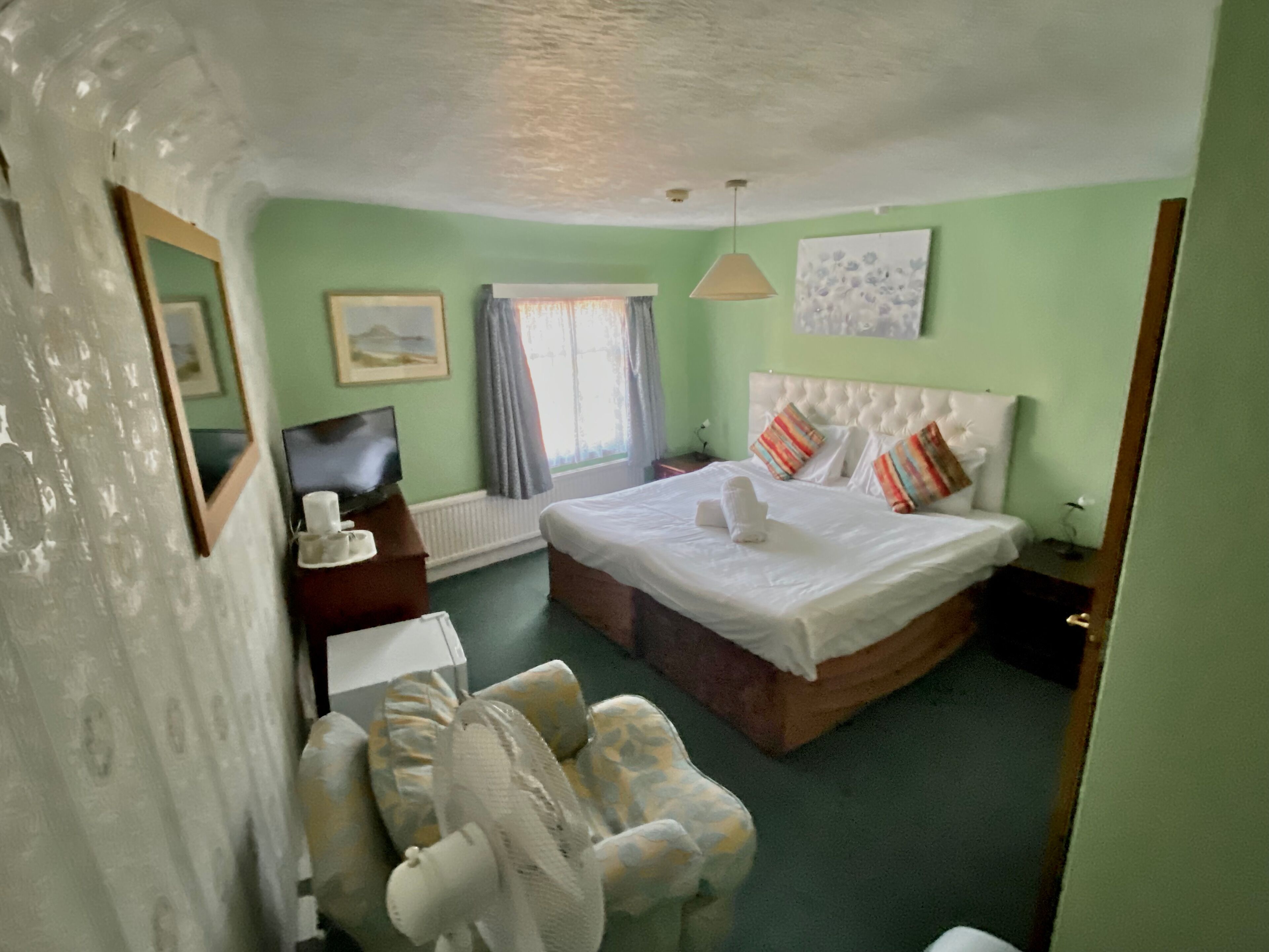 Een hotelkamer met een bed, een stoel, een bureau met een televisie en een raam met gordijnen.
