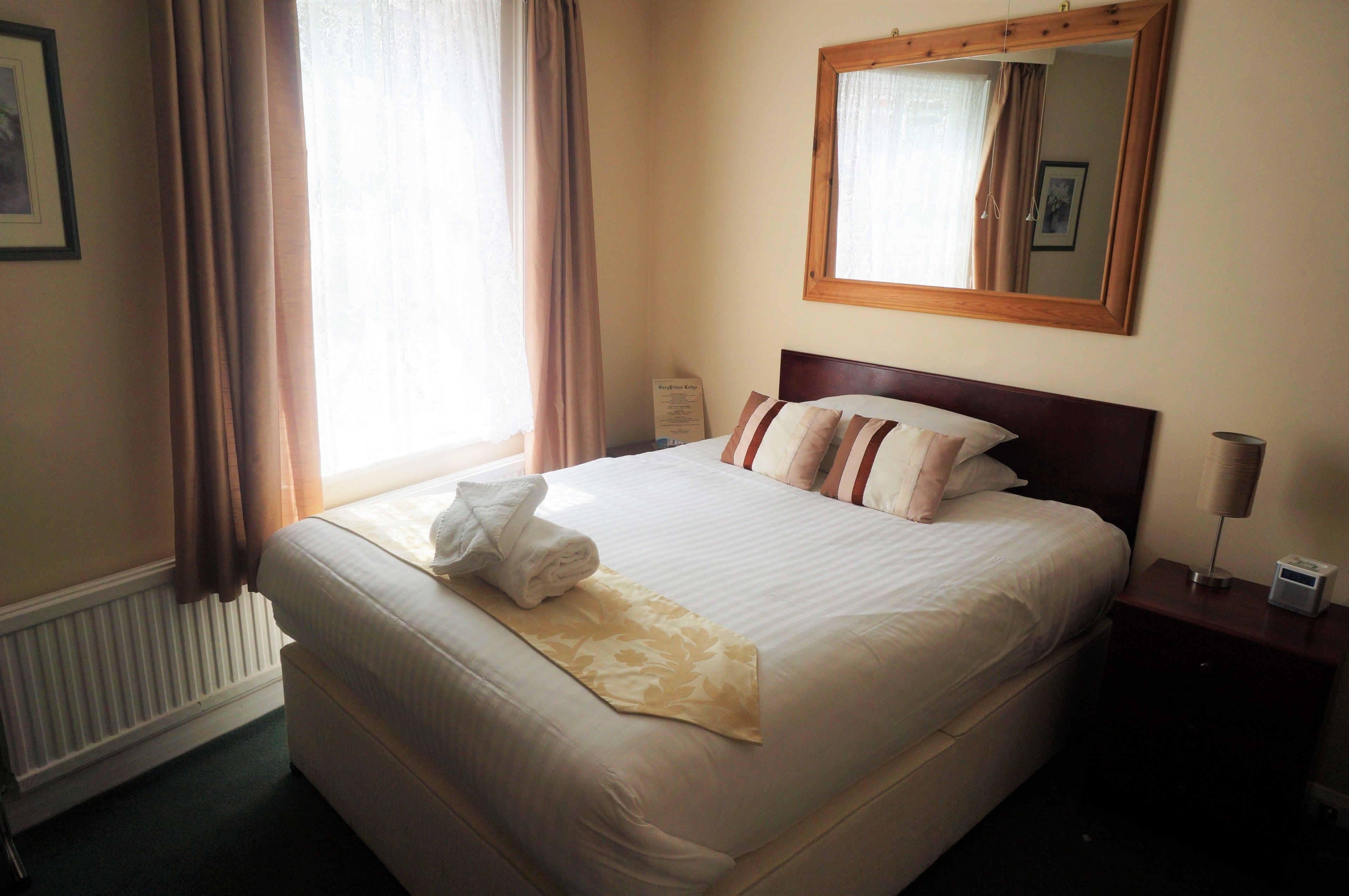 A neatly made bed with a white comforter and striped pillows, a bedside lamp, and a framed mirror on the wall.