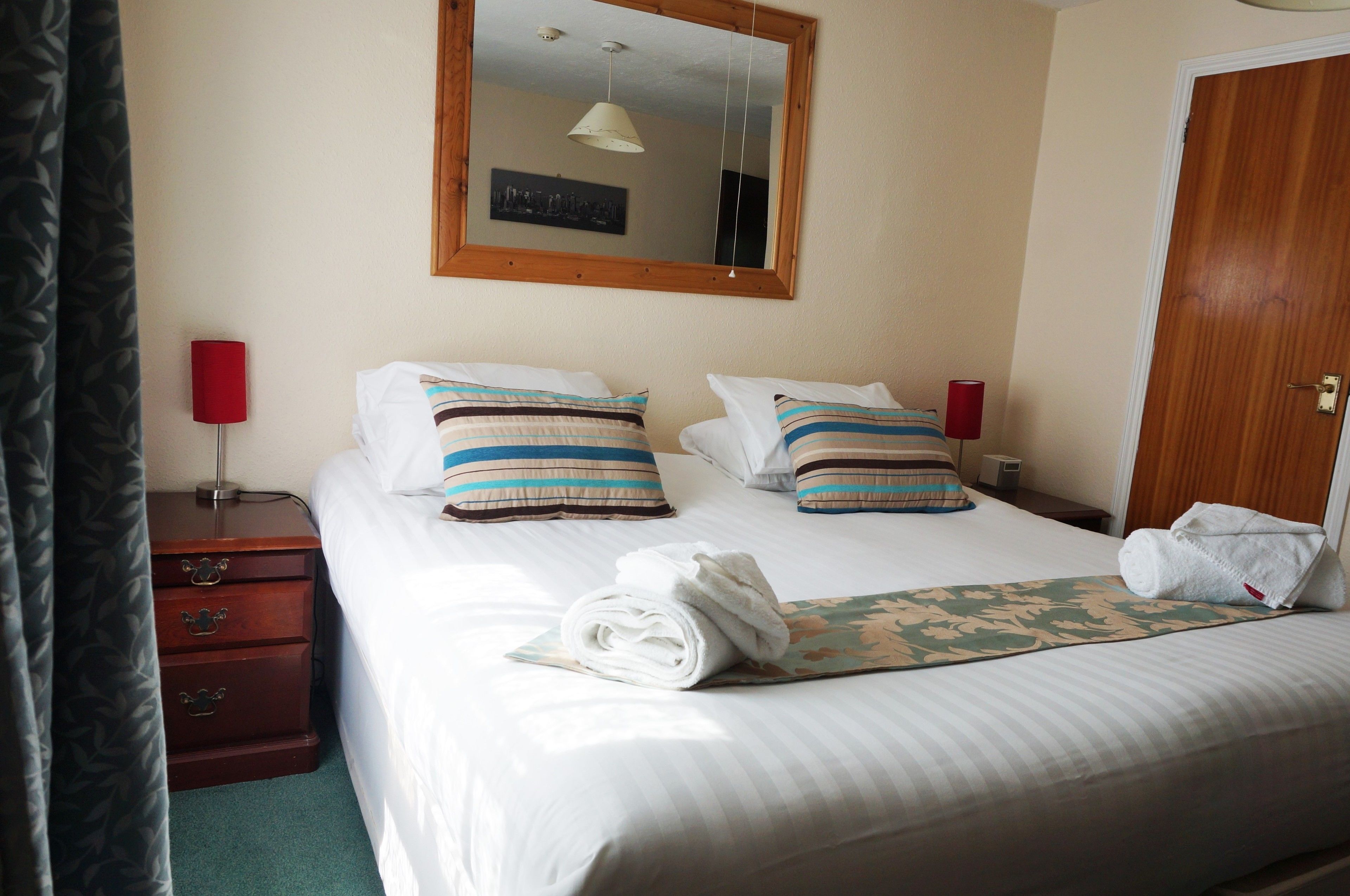 A neatly made bed with striped pillows, a folded towel, and a floral-patterned bedspread.