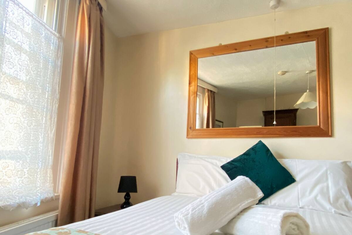 Una habitación de hotel con una cama bien hecha, un espejo grande y un ventanal con cortinas.