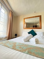 Una habitación de hotel con una cama bien hecha, un espejo grande y un ventanal con cortinas.