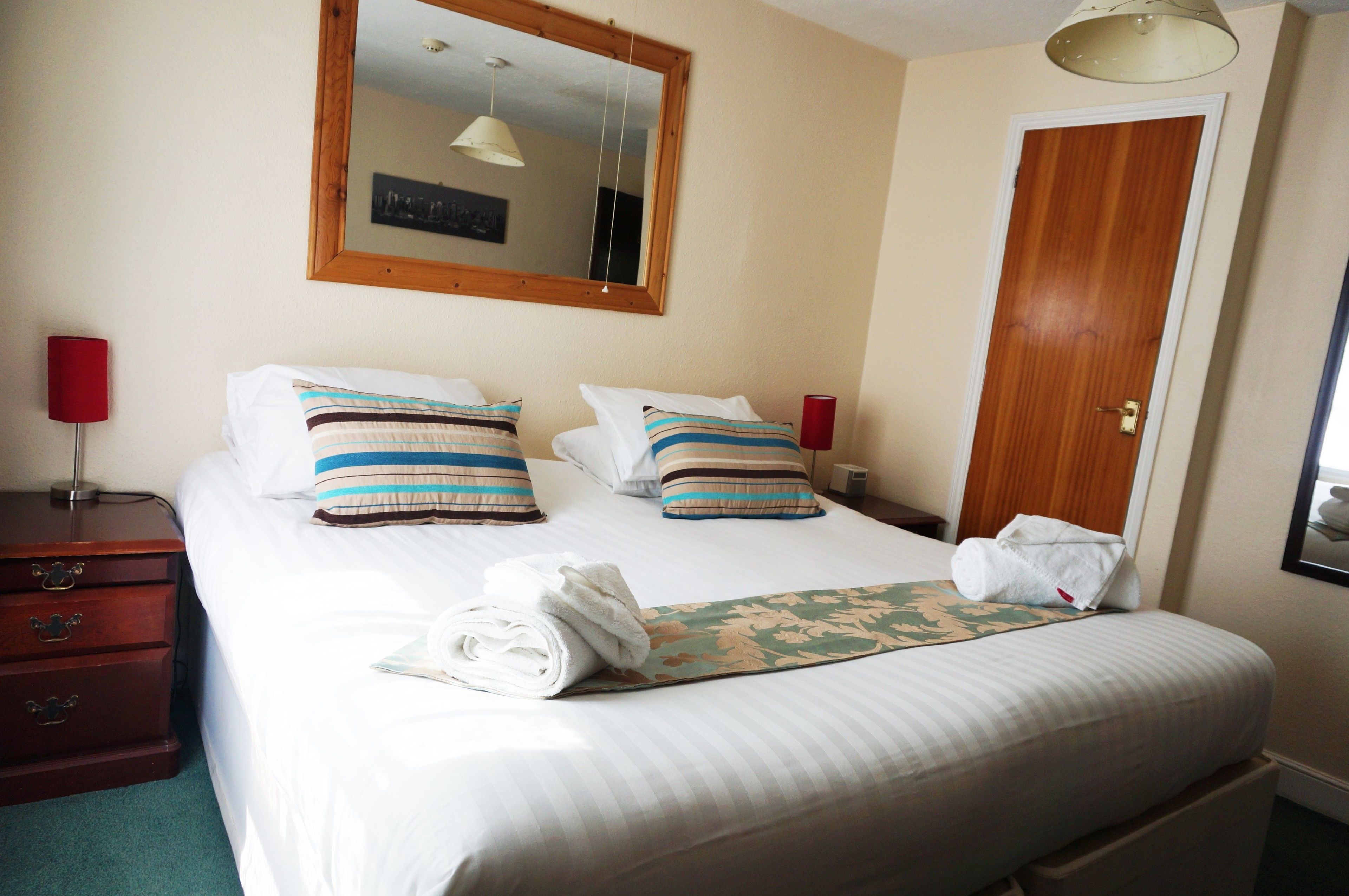 A neatly made bed with striped pillows, a folded towel, and a floral bedspread.