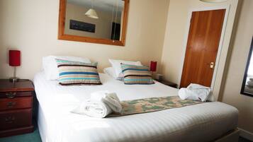 A neatly made bed with striped pillows, a folded towel, and a floral bedspread.