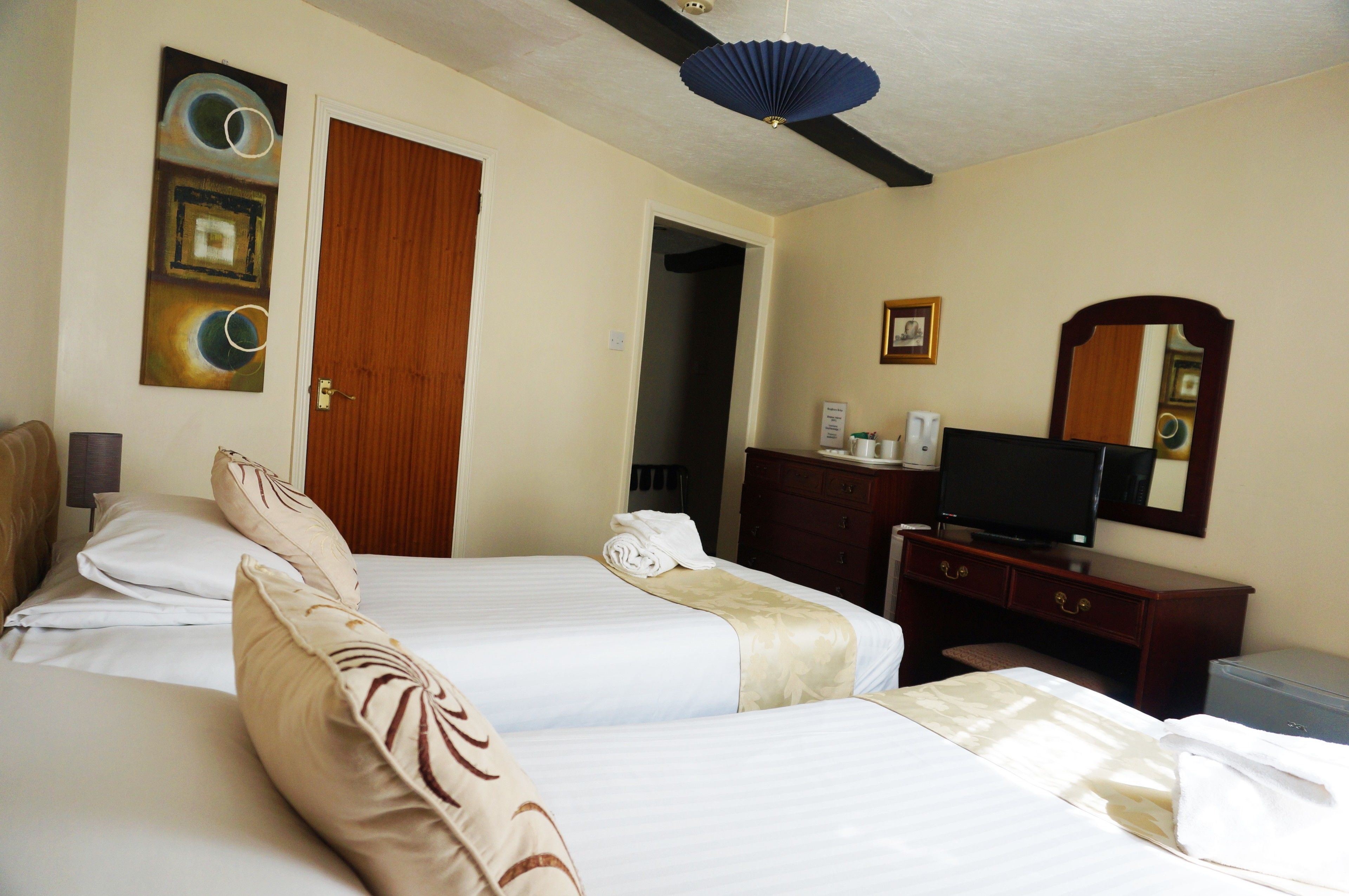 A hotel room with two beds, a wooden door, a desk with a television, and a mirror on the wall.