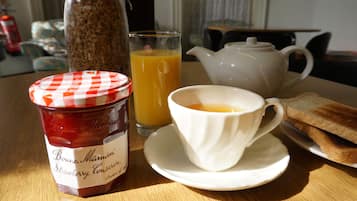 A breakfast setting with a jar of Bonne Maman strawberry conserve, a glass of orange juice, a teapot, and toast on a wooden table.