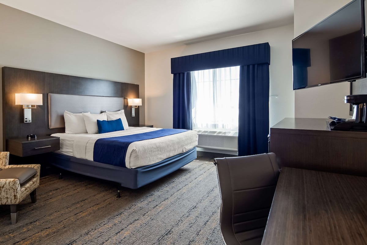A hotel room with a large bed, two bedside tables with lamps, a desk with a chair, a television, and a window with curtains.