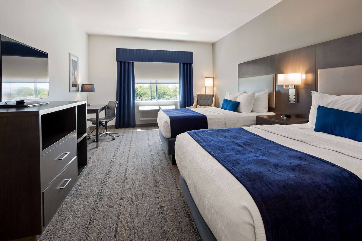 A hotel room with two beds, a desk, a chair, a TV, and a window with curtains.