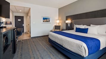 Habitación de hotel con una cama grande, un escritorio con lámpara, una silla y un cuadro en la pared.
